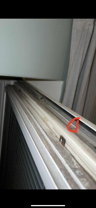 Närbild av ett fönster med sprucken glasruta, fokus på en krok och markerad del på överkanten av fönsterlisten.