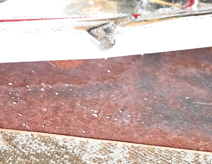 Närbild på en del av undergolvet och en vit matta som visar nivåskillnad och tjocklek efter borttagning av parkettgolv.