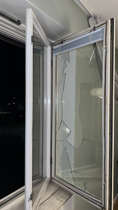 Öppet fönster med sprucket glas i innerfönstret, nattbild.