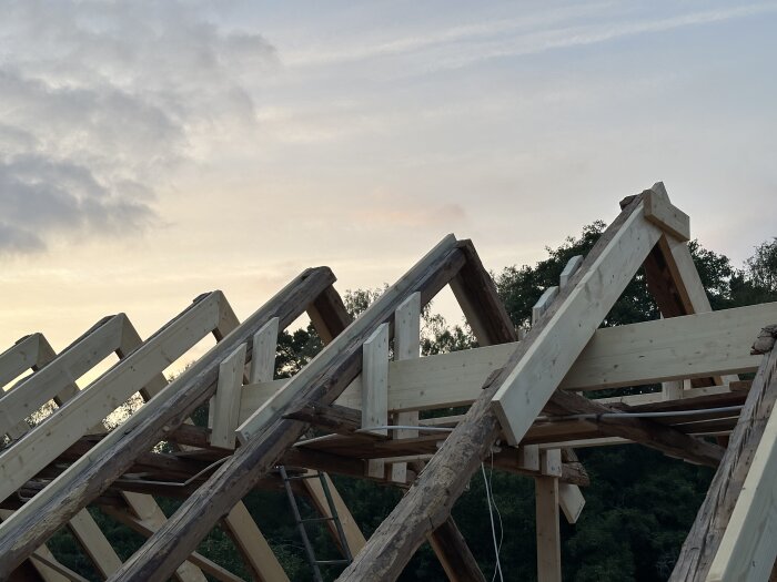 Takstolar och råspont i ett byggprojekt mot en solnedgång.