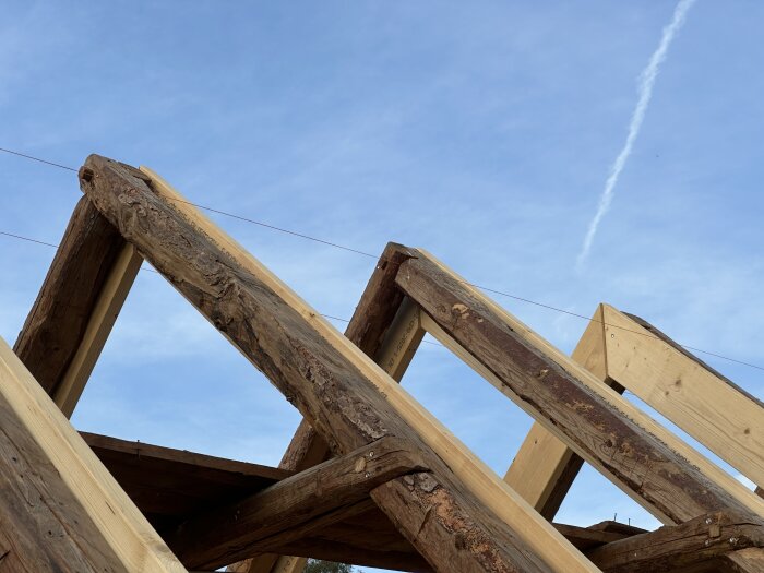 Takstolar av trä under konstruktion mot en klarblå himmel.