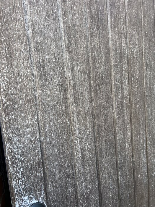 Sliten träyta av äldre dörr, troligen original från 1970-talet, behov av underhåll och oljebehandling, visas närbild av dörrens tillstånd.