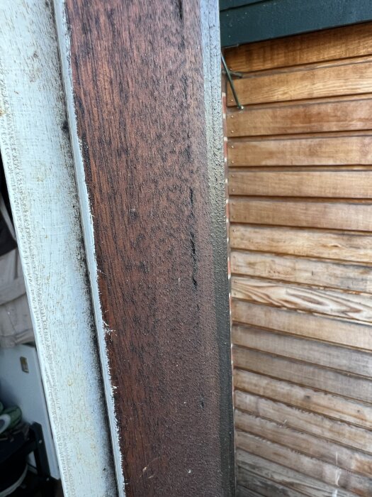 Närbild av äldre, sliten trä-ytterdörr från 70-talet, delvis inoljad och orörd, med kompletterande träpanel i bakgrunden.