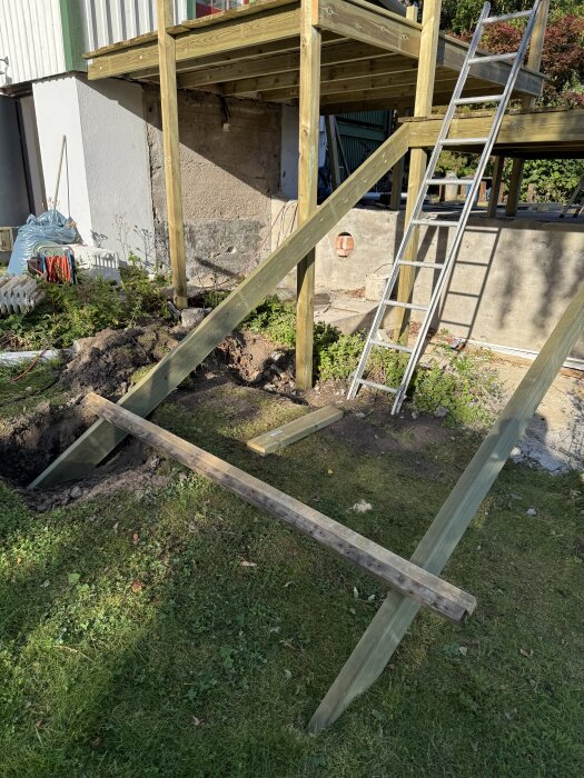 Byggprojekt av trappa från altan ner mot tomt. Stödstolpar och en stege syns, samt grävda och upphöjda jordnivåer vid suterräng.