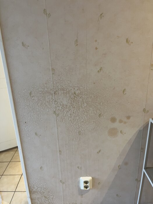 Fläckiga köksväggar med möjliga fuktskador, synliga mönster runt vägguttag; eventuellt påverkade av mögel eller vattenläckage.
