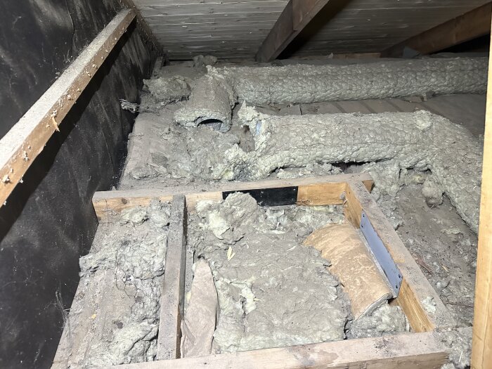 Isolerade frånluftskanaler på en vind med trästrukturer och exponerad isolering.