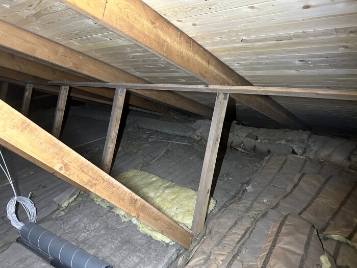 Bild av vinden med synliga ventilationskanaler och isoleringsmaterial under ett lutande tak av trä.