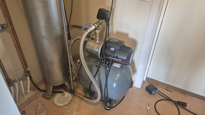 En pump installerad bredvid en metallcylinder, med rör och elkablar anslutna.