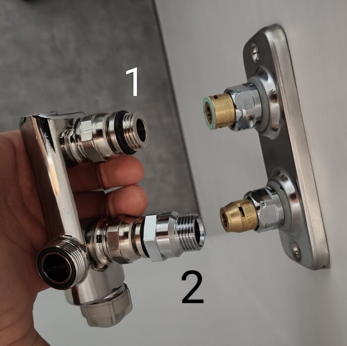 Hand som håller en etthålsventil nära en kopplingsbricka, märkta med siffrorna 1 och 2 för anslutningsmöjligheter.