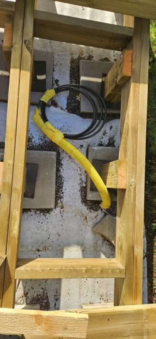 Under en träkonstruktion syns mark med kablar omslutna av gul plast, förberedelser för elinstallation.