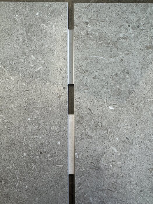 Grått kakel monterat med hårdfog, två plattor skilda med metallisk list.