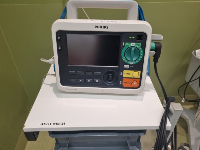 En defibrillator av märket Philips placerad på en vagn med texten "AKUT NISCH".