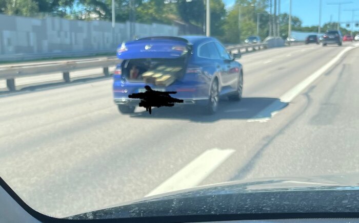 Blå bil med öppen bagagelucka lastad med tryckimpregnerad trästockar på väg.