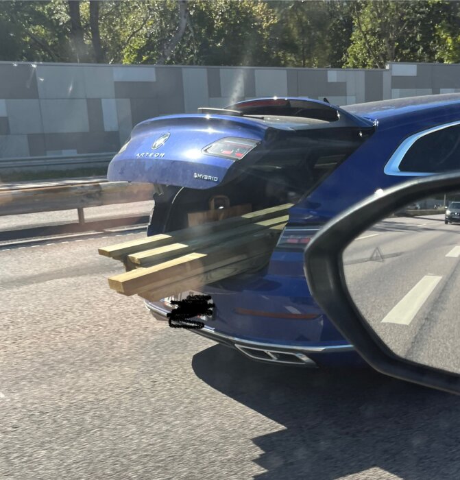Blå bil med bakluckan öppen, loss packad med tryckimpregnerade träreglar som sticker ut.