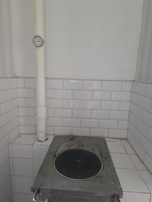 Vattenmantlad spis i hörnet av köket med rör och termometer; omgärdad av vit kakel.