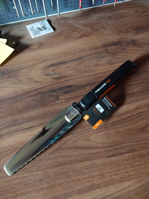 En handgrävare med taggigt blad på träbord, märkt "Fiskars". Verktyget används för att bekämpa ogräs i trädgården.