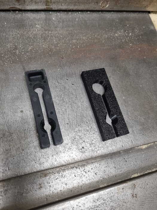 Två 3D-printade svarta fjäderanhåll i plast, placerade på en metallisk yta, designade för 24,8 mm spår.