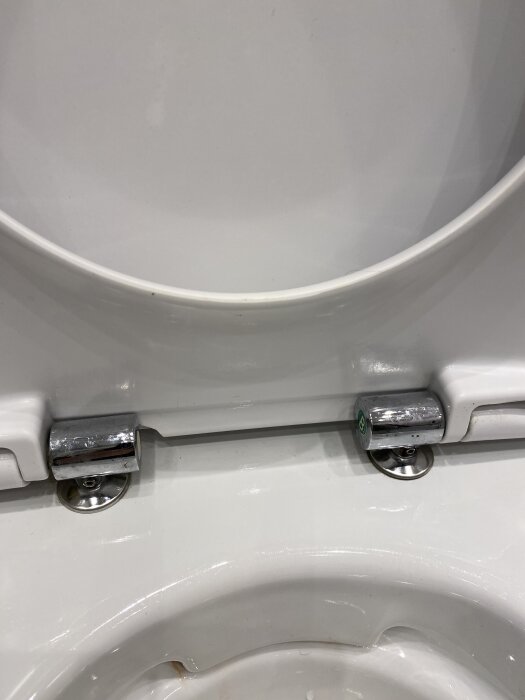 Toalettstol med närbild på fästena för sitsen, som sitter snett. Fästpunkterna sitter 15 cm från varandra.
