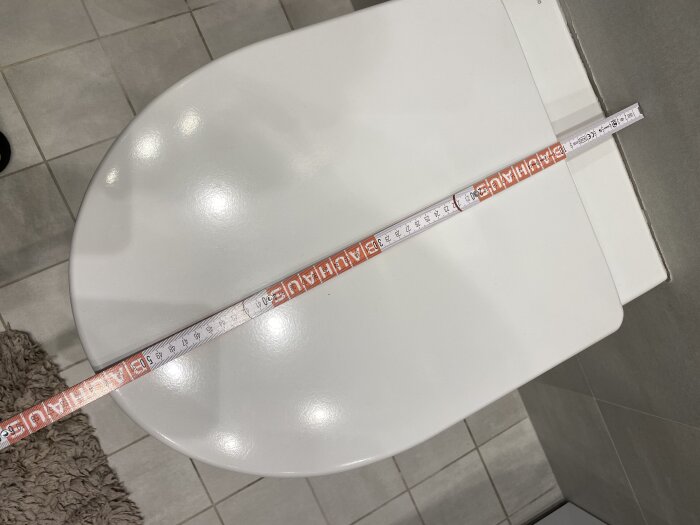 Toalettstol med en tumstock tvärs över locket, längd visas som 36 cm.