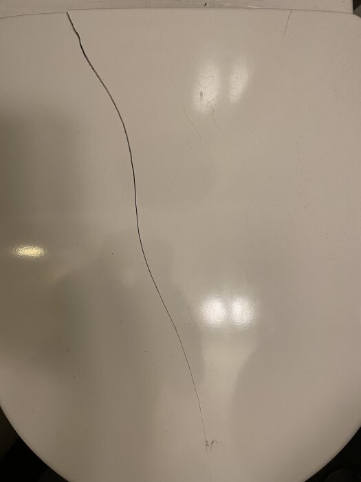 Sprucken toalettsits i Gustavsberg Arctic toalettstol, med bred och tunn spricka synlig på ytan.