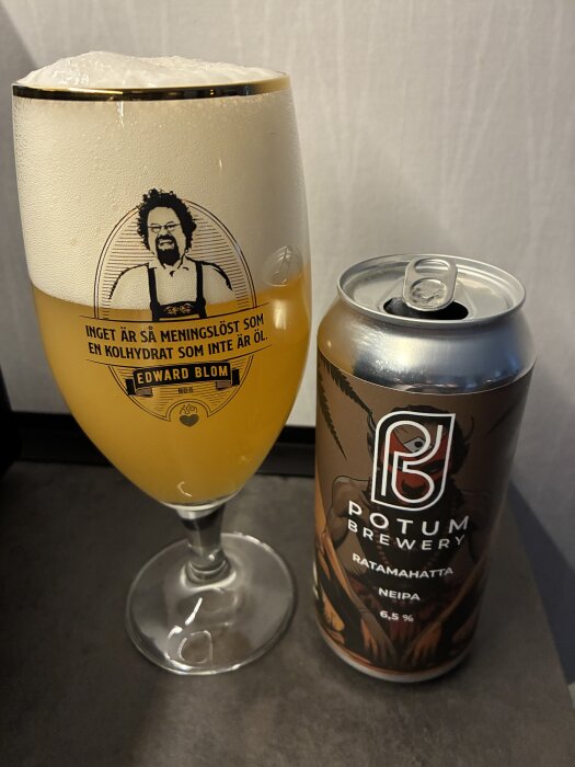 Ett glas öl med skum och etikett med Edward Blom-bild samt en burk Potum Brewery Ratamahatta NEIPA, 6,5% alkohol.
