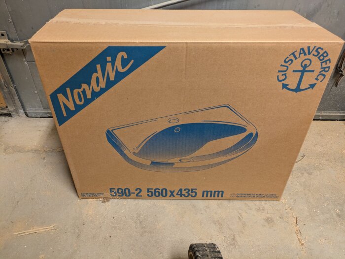 Kartong med Gustavsberg Nordic tvättställ, modell 590-2, 560x435 mm, från slutet av 90-talet, i ett garage.