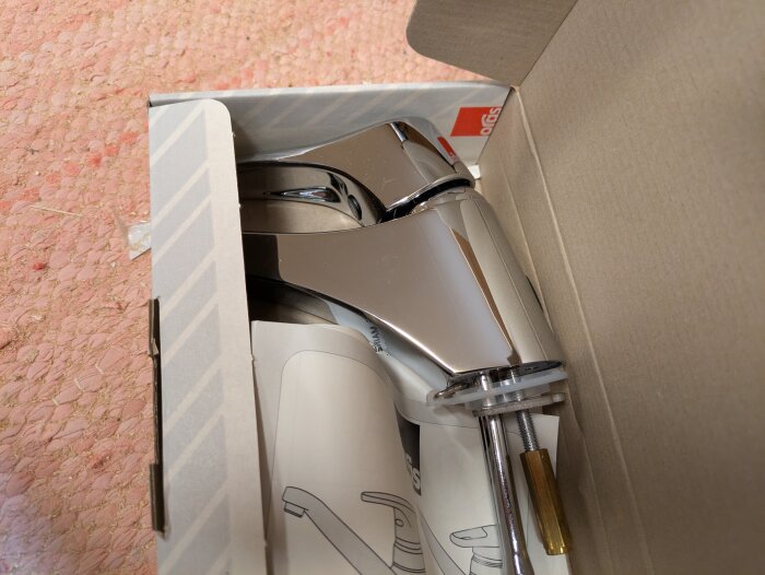 Kromfärgad blandare i en öppnad kartong på rosa matta, del av garageutrensning, till försäljning.