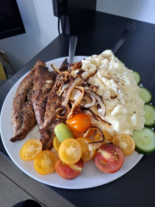 Stekt makrill med lök, potatismos, gurkskivor och tomater pÄ en tallrik.