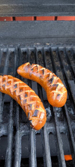 Två grillade korvar med rutnätsskåror ligger på en svart grill.