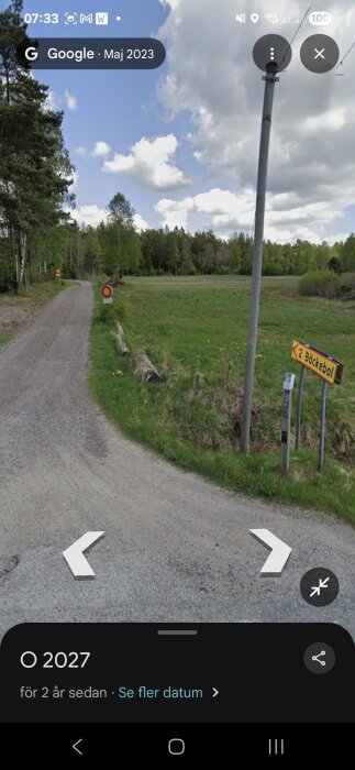 Grusväg med förbudsskylt och skylt mot Bäckebol, grönska och skog i bakgrunden under en molnig himmel.