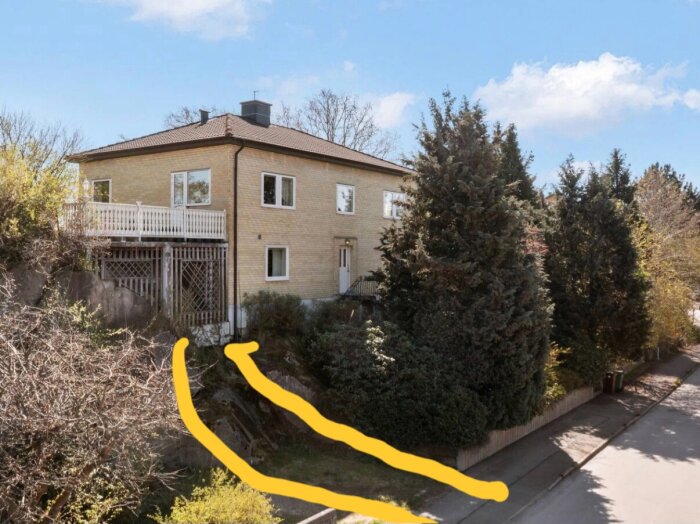 Hus med träaltan och pelare, omgiven av träd, med gula markeringar som visar möjlig framtida asfalteringsområde.