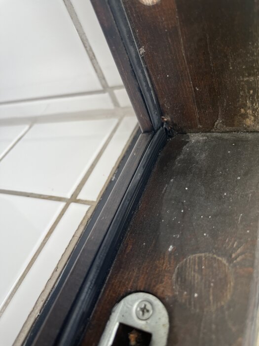 Gummilist monterad längs kanten av ett träfönster, med kakelplattor synliga i bakgrunden.