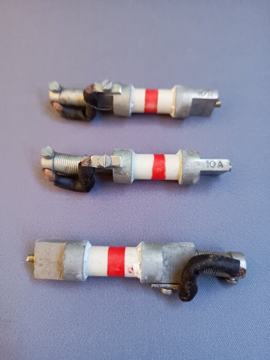 Ovanliga säkringar med fjäderbelastat kontaktstift och röd markering, visas i tre exemplar på en grå yta.