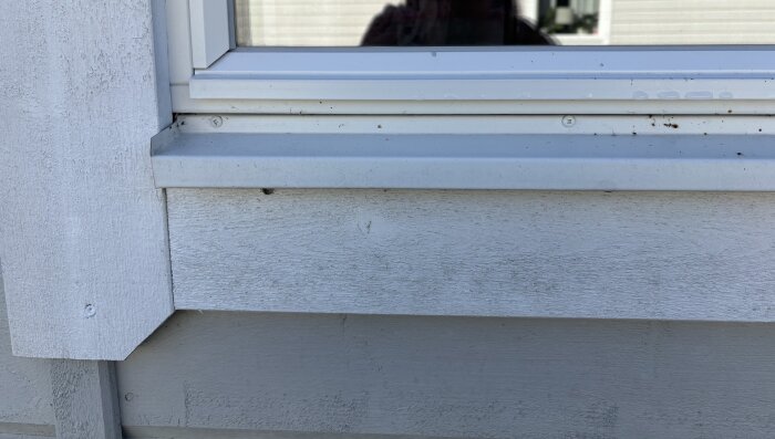 Ikkunalauta ja seinäpaneeli ulkopuolelta kuvattuna, vaaleanharmaa maalipinta ja valkoinen ikkunakehys.