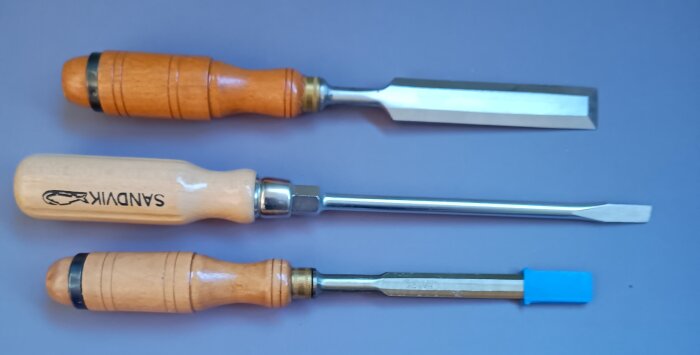 Träverktyg med träskaft, tre skruvmejslar från olika märken på lila bakgrund.