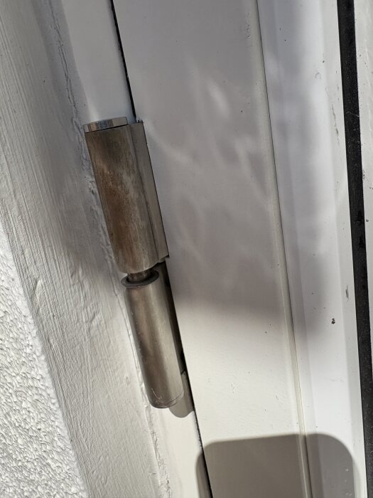 Gångjärn på en vit altandörr med synliga tecken på slitage eller rost.