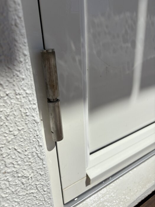 Gångjärn på en vit altandörr med synlig slitage och missfärgning, fotograferat nära husfasad.