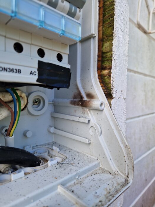 Blöt elcentral på yttervägg med misstänkt elbrandskada, synliga kablar och smuts vid säkringsboxens öppning.