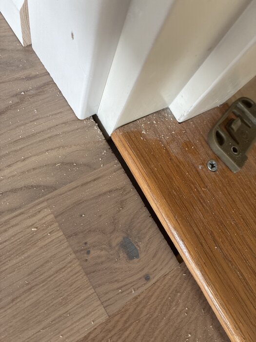 Hålrum mellan golvbräda och tröskel, träspån synliga.