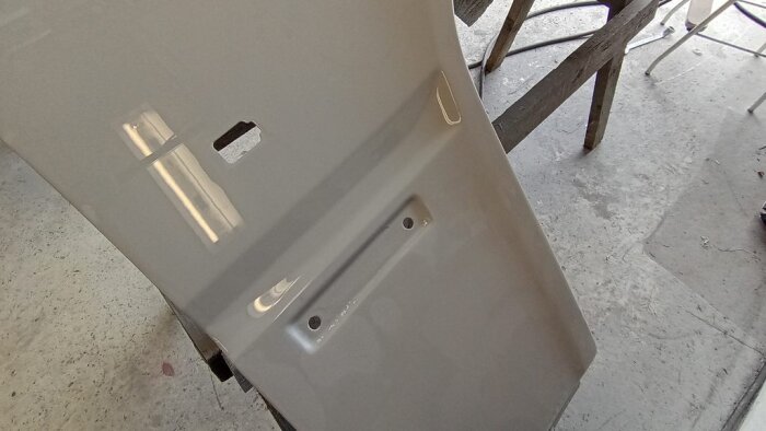Nymålad bilskärm efter våtslipning och färgläggning, lyser i ljuset, placerad i ett garage med verktyg och arbetsbänk i bakgrunden.