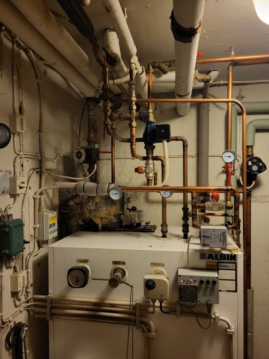 Panna med kopparrörsinstallation i källare, mätare och ventiler synliga; tecken på tidigare demonterat system.