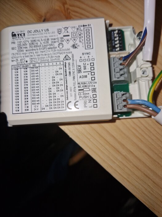 LED-drivdon av märket TCI med etikett och inkopplade elektriska kablar ligger på ett trägolv.