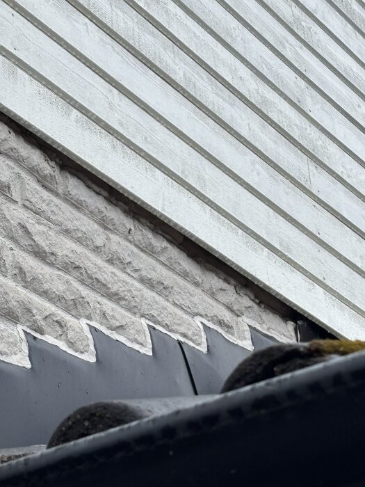 Liggende träpanel möter tegel på en gavelspets med takpannor i förgrunden, fråga om underbleck behövs mellan panel och tegel.