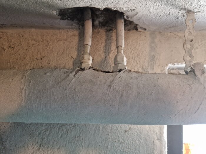 En murad vägg med rörledningar som sticker ut genom en öppning i väggen, täckta med skyddande material.