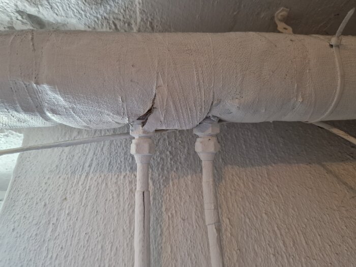 Sprucken rörledning med målade och lindade kopplingar i taket.