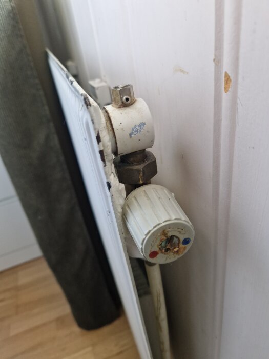 En närbild av en vit radiator monterad mot en vit vägg, med ett ventilsystem och en vit termostatknapp.