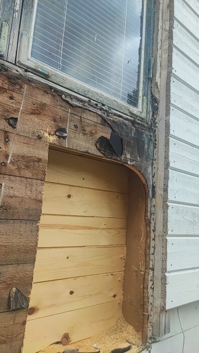 Öppning i en vägg där en altandörr ska installeras, med synligt trä och borttagen puts runt fönsterkarm.