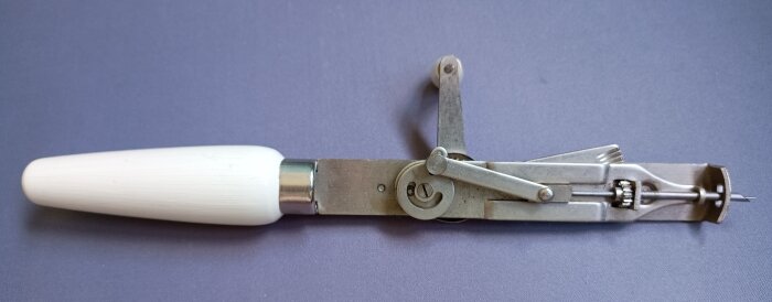 Verktyg med trähandtag och metallmekanism för handtillverkning av ryamattor, placeras mot lila bakgrund.