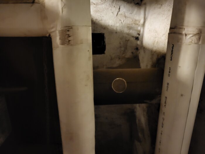 Rörsystem med isolerade vita rör och ett mörkare rör som kan vara platsen för en analog rökgastermometer på baksidan av en panna.