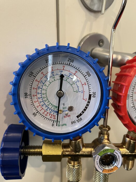 Manometer med blå ram visar tryck och temperatur, del av mätinstrument för kylsystem.